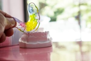 Colorful orthodontic retainer held above a dental model, representing BZ Orthodontics' treatment options in Lansdale, PA, including Invisalign and braces.