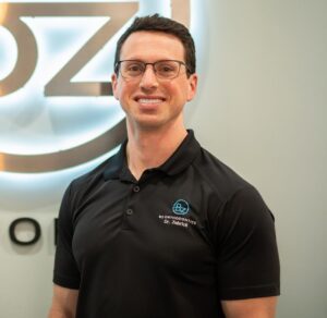 Dr. Brian Zebrick smiling in a black polo shirt with BZ Orthodontics logo, standing in front of a branded backdrop, promoting patient connection and consultation opportunities.