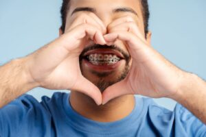 Smiling young man with braces making a heart shape with his hands, promoting orthodontic care at BZ Orthodontics in Lansdale, PA.