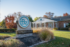 BZ Orthodontics office exterior featuring sign with Dr. Brian Zebriek, surrounded by greenery, showcasing Lansdale location for braces and Invisalign services.