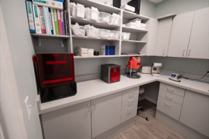 Orthodontic office workspace at BZ Orthodontics in Lansdale, featuring organized shelves with dental supplies, a 3D printer, and equipment for braces and Invisalign treatments.