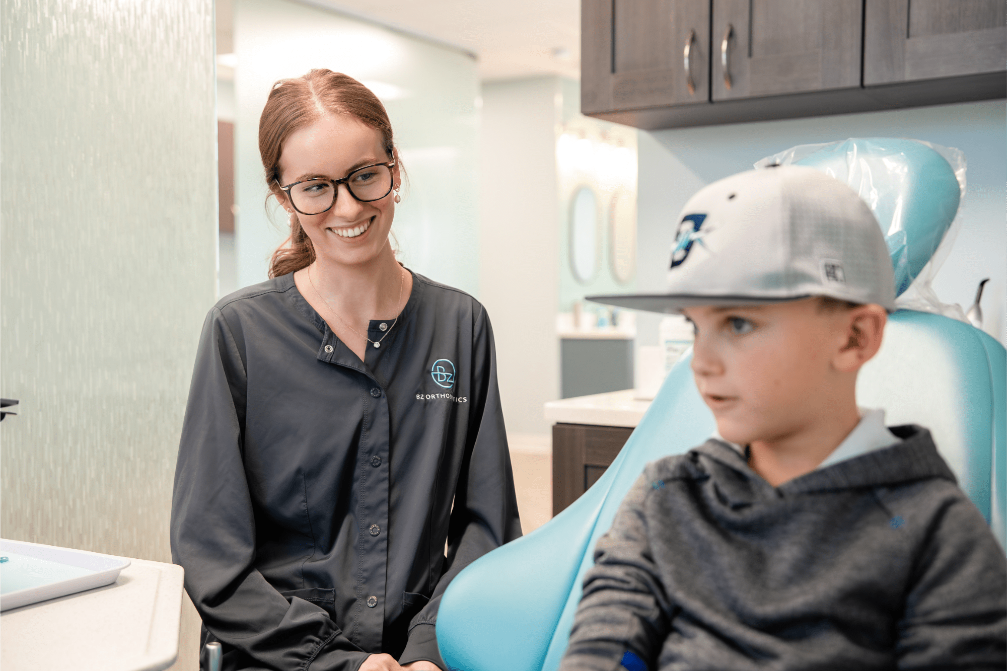 Orthodontist at BZ Orthodontics smiling with young patient in a dental chair, promoting affordable braces and Invisalign options in Lansdale, PA.
