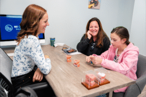 Two women and a girl sitting at a table discussing orthodontic options, with BZ Orthodontics branding visible in the background, showcasing a friendly consultation atmosphere related to Invisalign and braces in Lansdale.