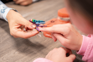 Hand holding colorful orthodontic braces component, child&rsquo;s hand reaching out, BZ Orthodontics patient experience, Dr. Zebriek, Invisalign Lansdale, Lansdale braces, orthodontist Lansdale PA.