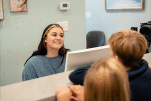 Smiling receptionist at BZ Orthodontics assisting patients, showcasing friendly service in an inviting office environment.