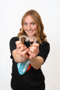 Smiling orthodontic team member at BZ Orthodontics holding Invisalign aligners in a heart shape, promoting orthodontic care in Lansdale, PA.