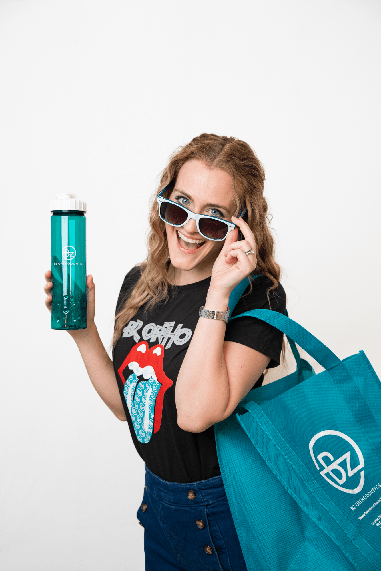 bz ortho-team-headshots-fun-11 Smiling woman wearing sunglasses, holding a turquoise water bottle and a teal tote bag with BZ Orthodontics logo, showcasing a fun and friendly atmosphere at BZ Orthodontics, promoting patient engagement and comfort in orthodontic care.