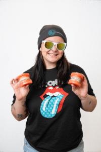 Fun headshot of a BZ Orthodontics team member wearing a Rolling Stones shirt and sunglasses, holding orange containers, promoting a friendly atmosphere in orthodontics.