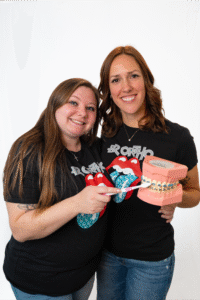 Two smiling team members from BZ Orthodontics holding a model of braces and toothbrush, promoting friendly orthodontic care in Lansdale, PA.