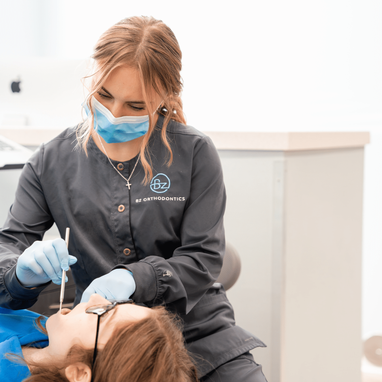 Orthodontic assistant in a face mask working on a patient's braces in the treatment chair