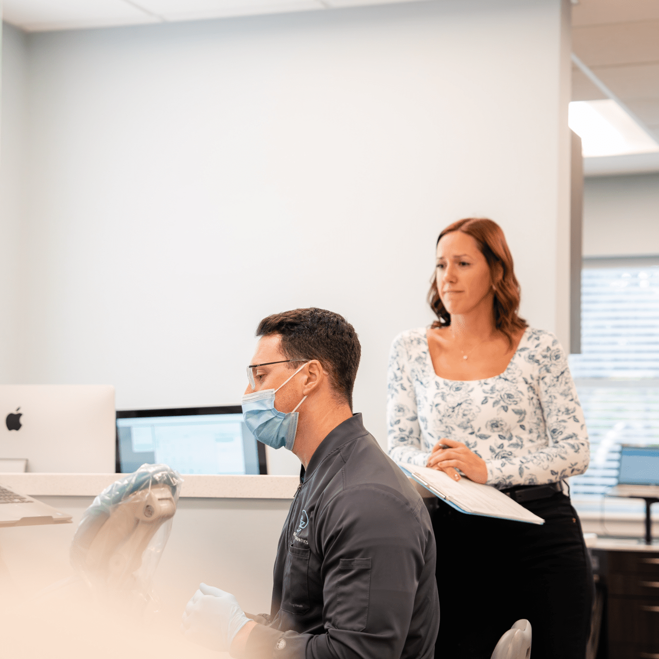 Orthodontist in a face mask working at a computer while a team member reviews notes beside him