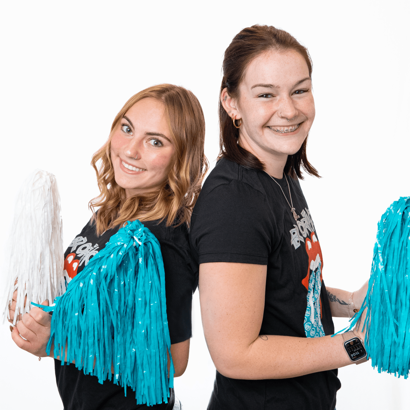 Two young women smiling back-to-back, holding colorful pom-poms, promoting BZ Orthodontics and a friendly atmosphere for orthodontic care in Lansdale, PA.