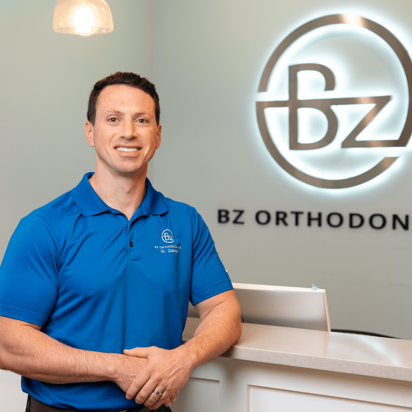 Dr. Brian Zebrick in blue polo shirt at BZ Orthodontics reception, showcasing a welcoming environment for orthodontic care in Lansdale, PA.