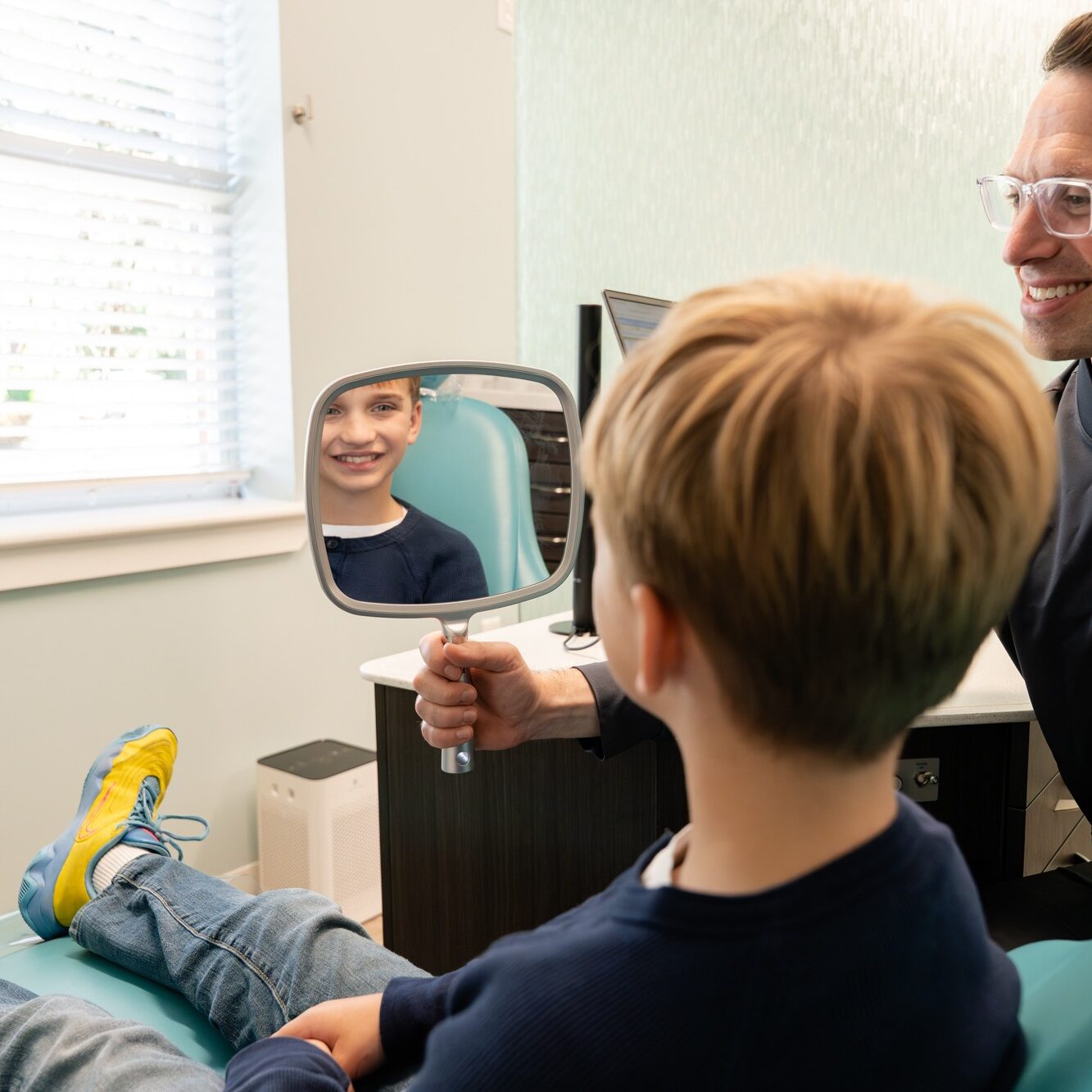 Child smiling in a dental chair while looking into a mirror held by an orthodontist, showcasing a positive orthodontic experience at BZ Orthodontics in Lansdale.
